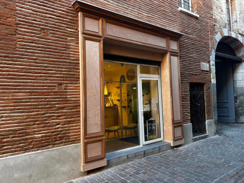 Façade rénovée avec vitrine en bois sur une rue pavée. La menuiserie élégante contraste avec le mur de briques rouges d'une vieille ville.