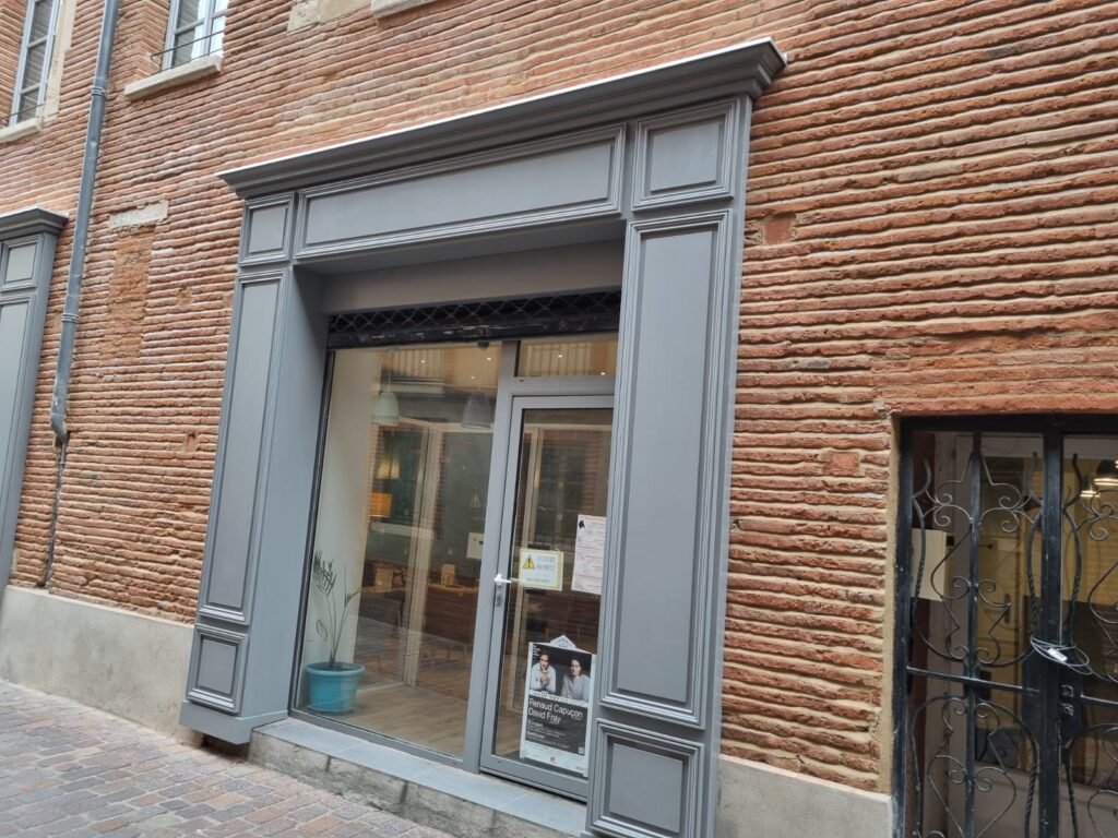 Façade historique en briques rouges texturées. Vitrine et porte vitrée avec encadrement gris mouluré. Affiche Renaud Capuçon David Fray.