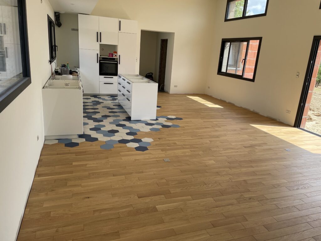 Cuisine blanche neuve avec four intégré. Sol unique : parquet chêne clair et carrelage bleu hexagonal "éclaté" vers le séjour.